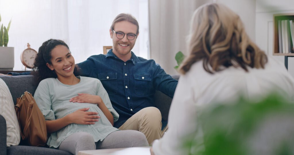 Ein Paar bei der geburtspsychologischen Beratung, sitzt auf einer Couch und redet miteinander.