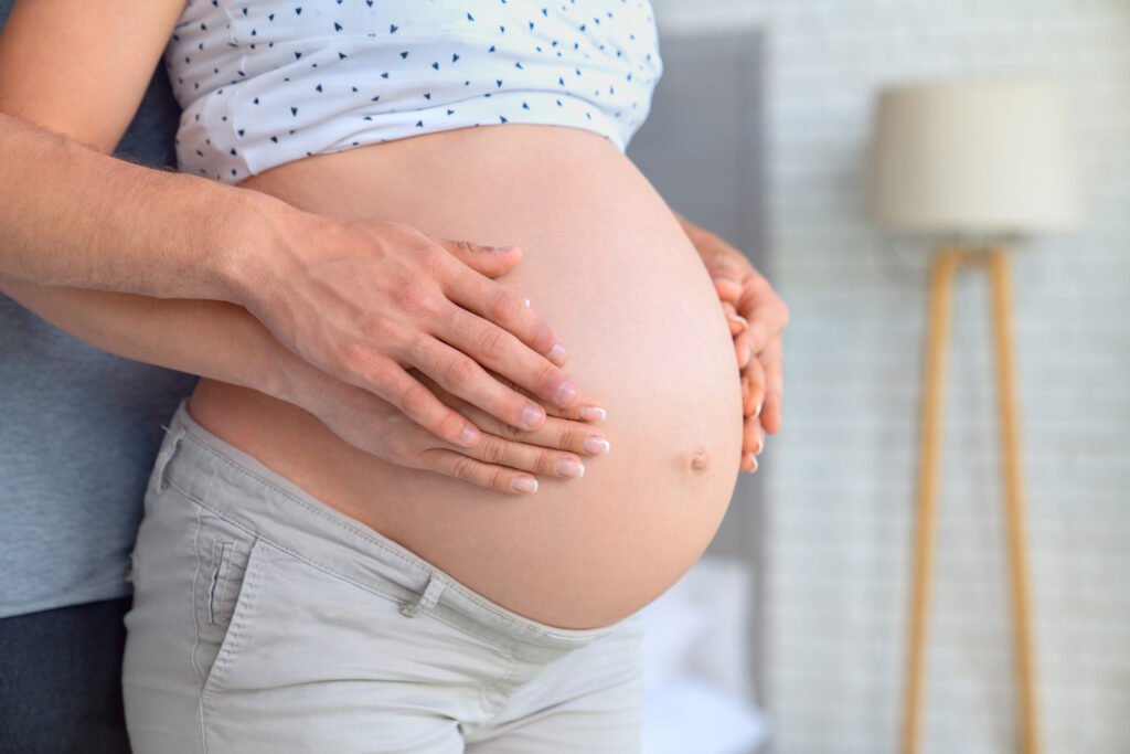 Close up of parents hands touching pregnant belly at home