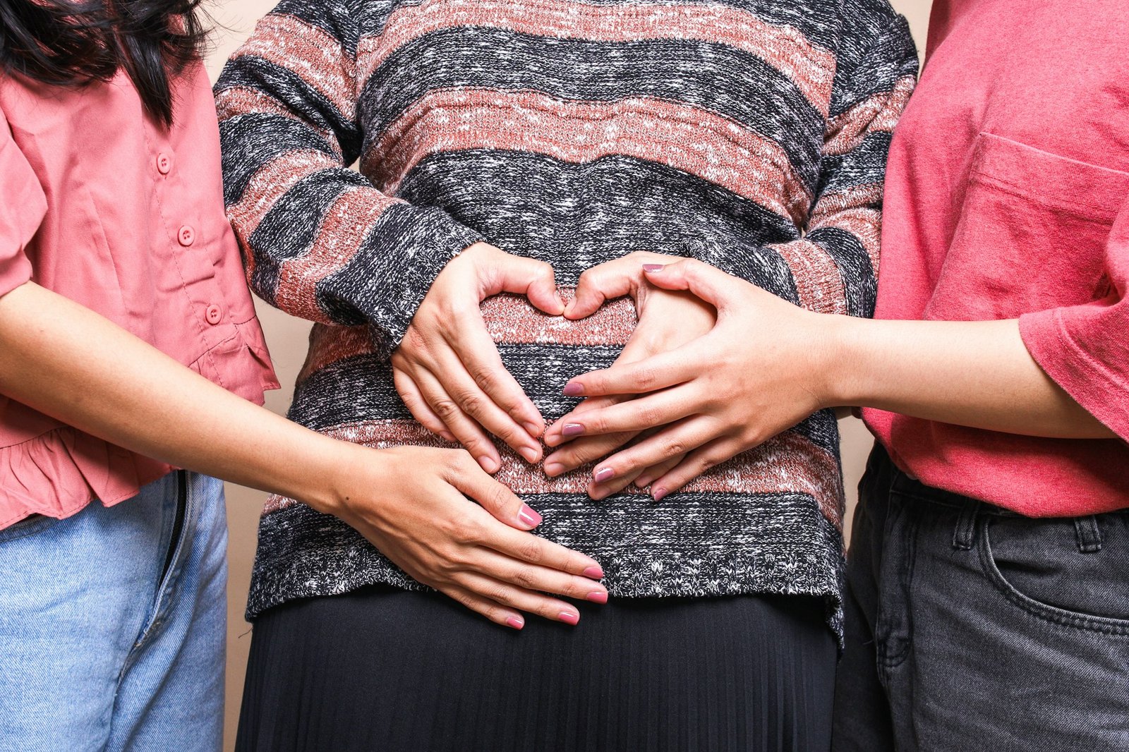 Drei Personen bilden mit ihren Händen eine Herzform um den schwangeren Bauch in der Tradition der Geburtskultur.